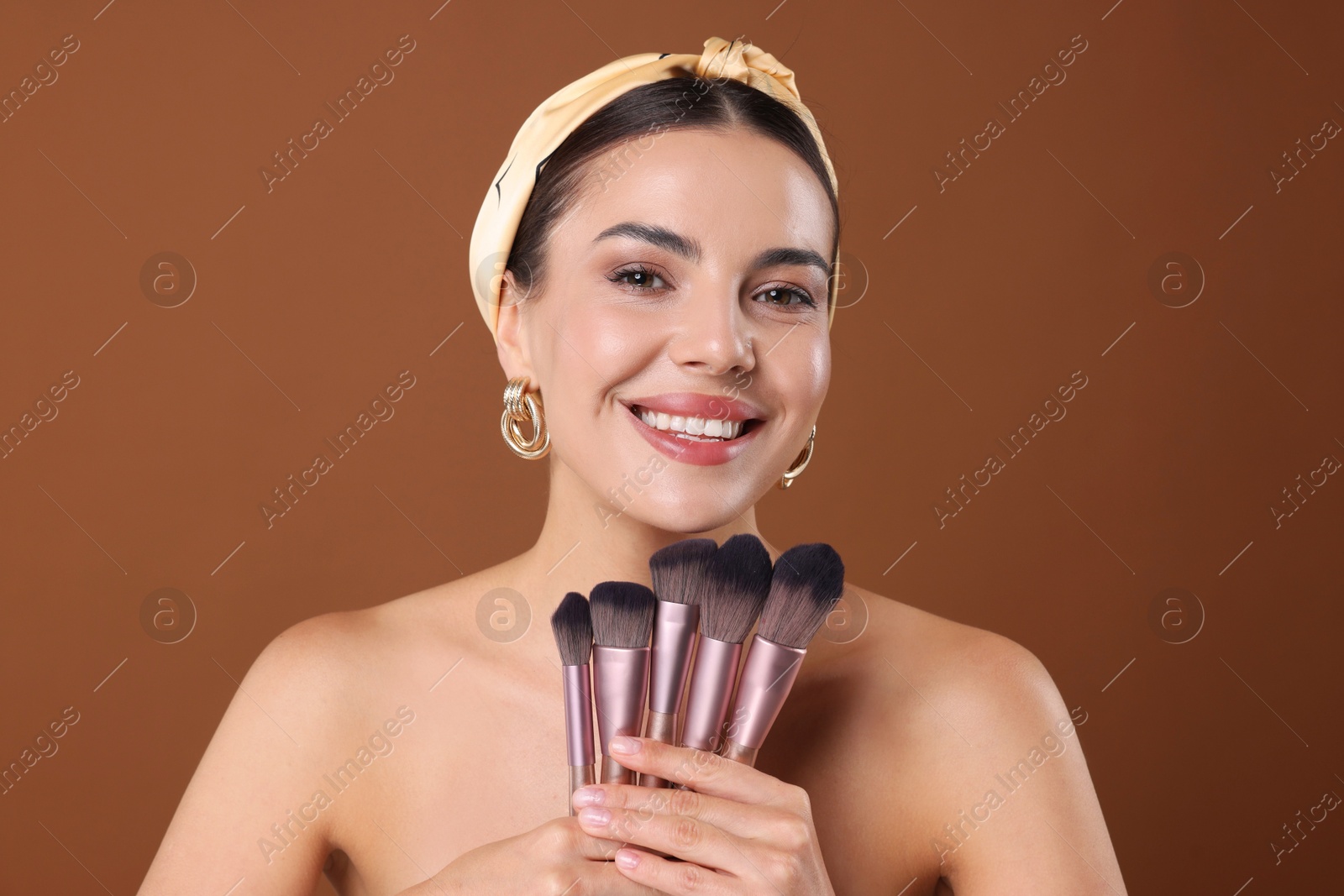 Photo of Beautiful woman with makeup brushes on brown background
