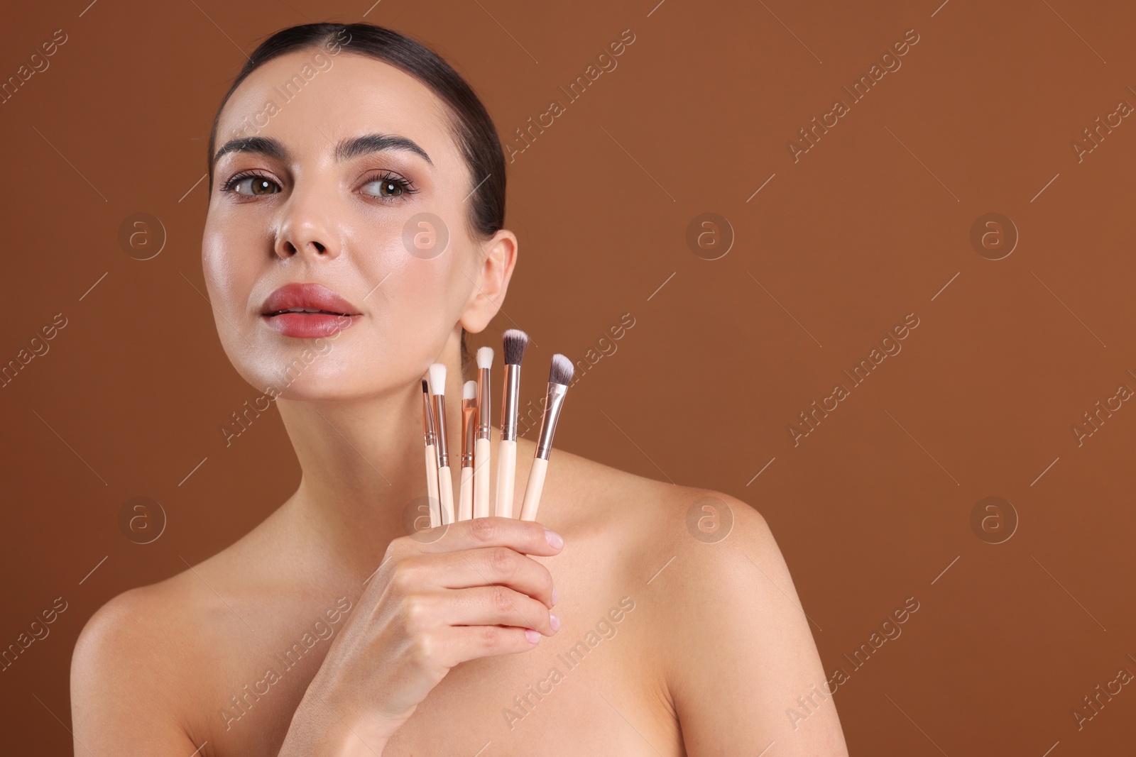 Beautiful woman with makeup brushes on brown background, space for text Photo of Beautiful woman with makeup brushes on brown background, space for text