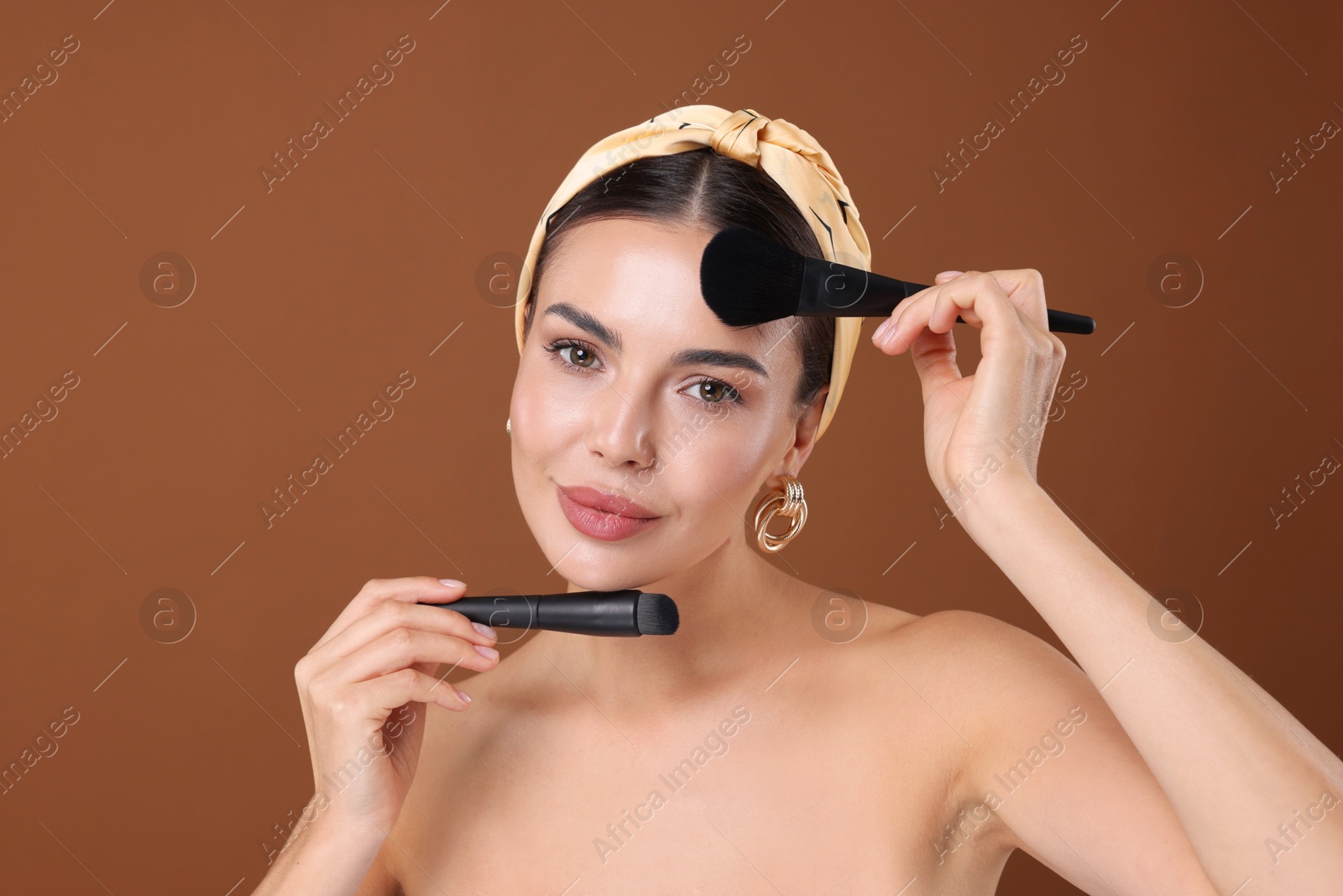Photo of Beautiful woman with makeup brushes on brown background