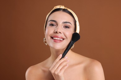 Photo of Beautiful woman with makeup brush on brown background