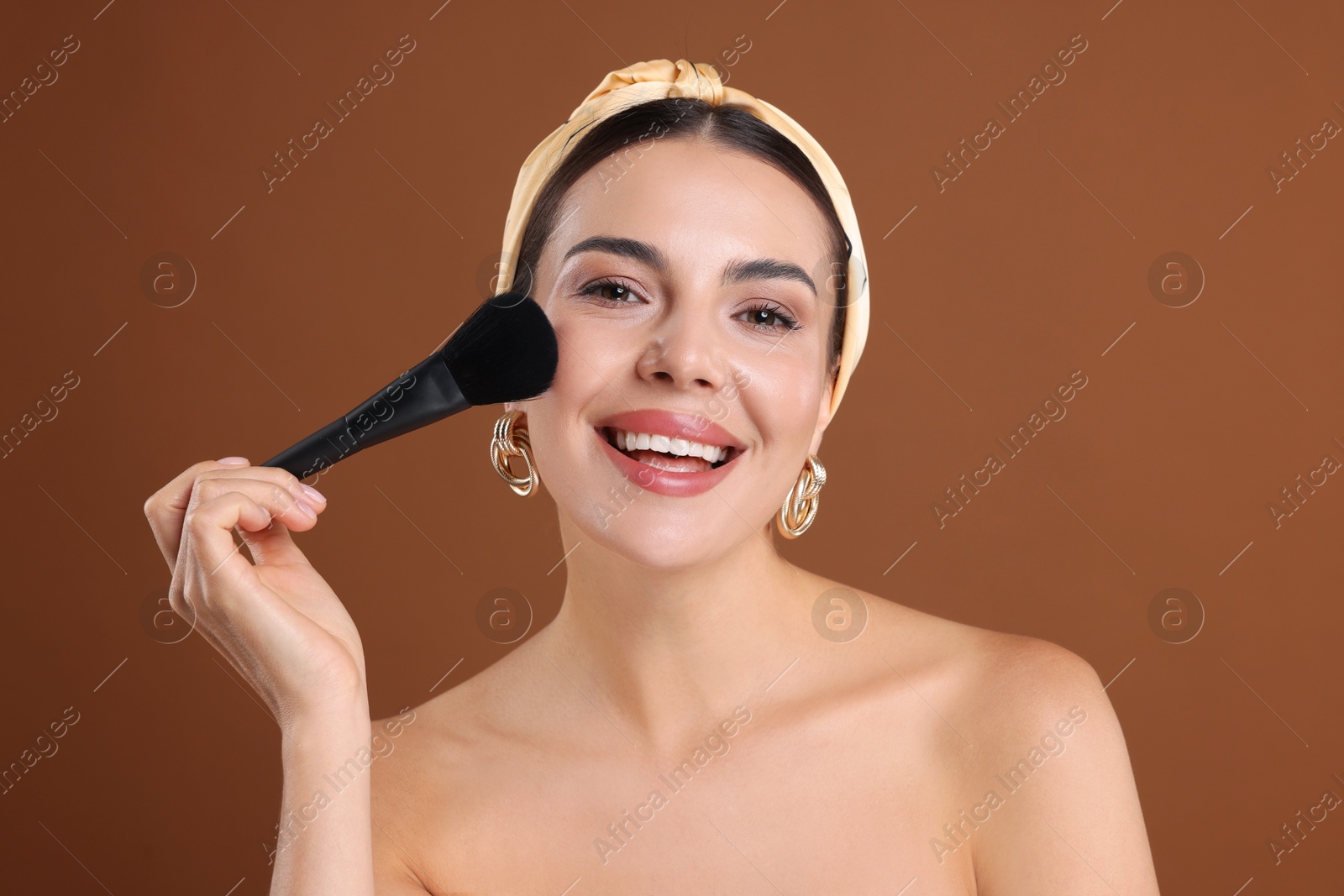 Beautiful woman applying makeup with brush on brown background Photo of Beautiful woman applying makeup with brush on brown background