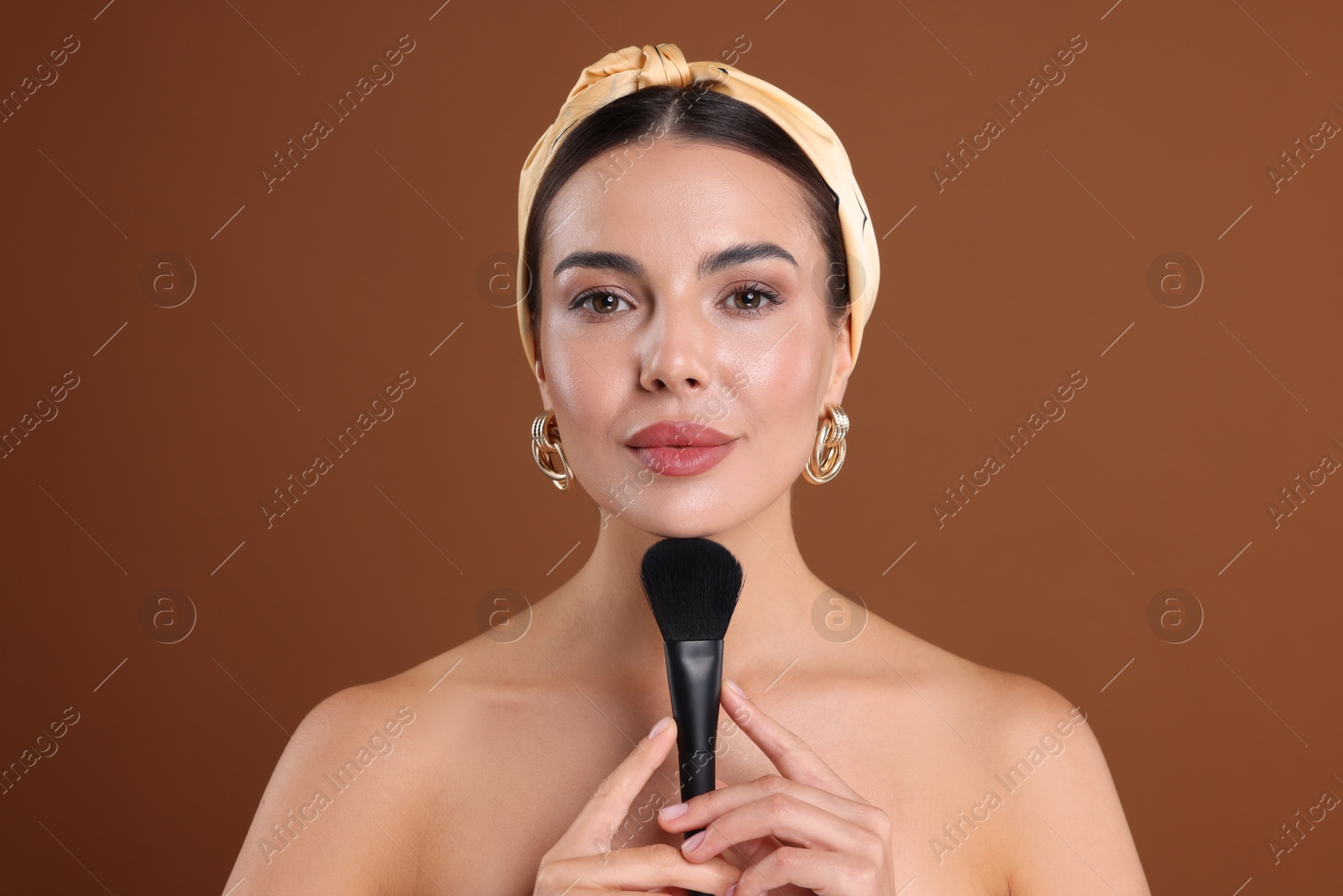 Beautiful woman with makeup brush on brown background Photo of Beautiful woman with makeup brush on brown background
