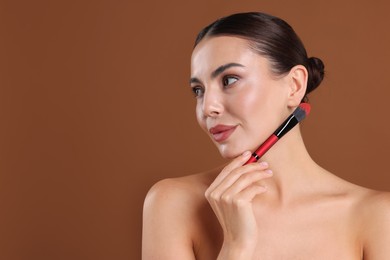 Photo of Beautiful woman with makeup brush on brown background, space for text