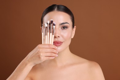 Photo of Beautiful woman with makeup brushes on brown background