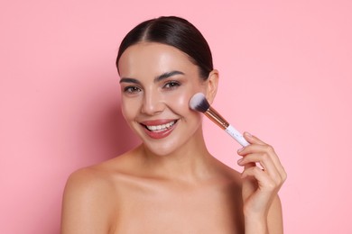 Photo of Beautiful woman applying makeup with brush on pink background