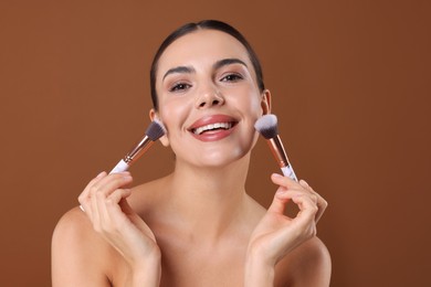 Photo of Beautiful woman with makeup brushes on brown background
