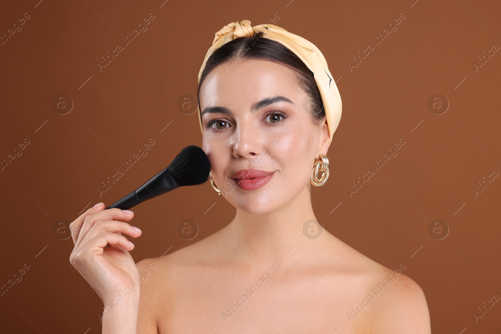 Beautiful woman applying makeup with brush on brown background Photo of Beautiful woman applying makeup with brush on brown background
