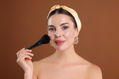 Photo of Beautiful woman applying makeup with brush on brown background