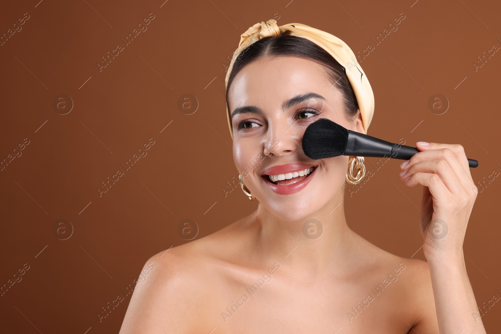 Beautiful woman applying makeup with brush on brown background, space for text Photo of Beautiful woman applying makeup with brush on brown background, space for text