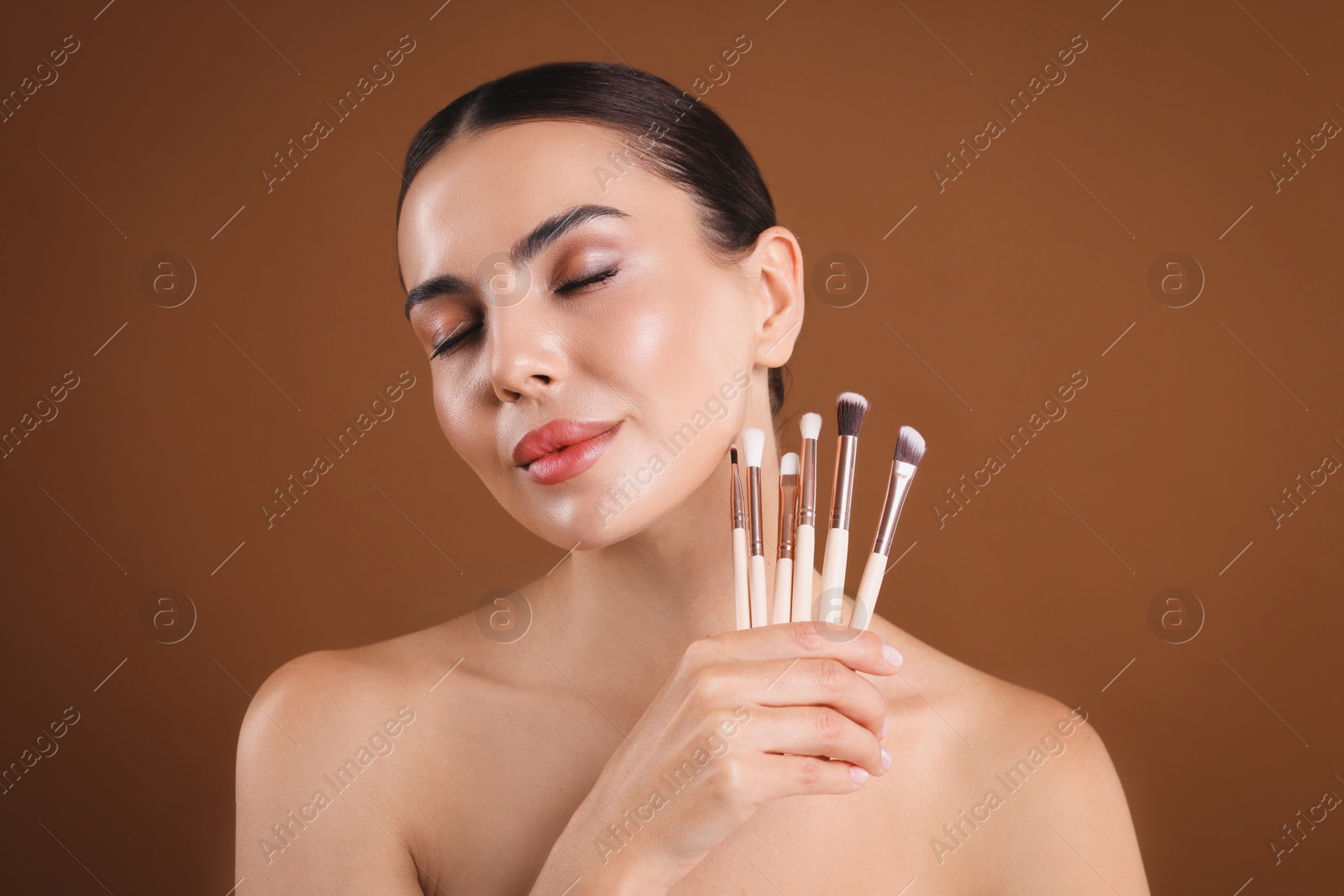 Beautiful woman with makeup brushes on brown background Photo of Beautiful woman with makeup brushes on brown background