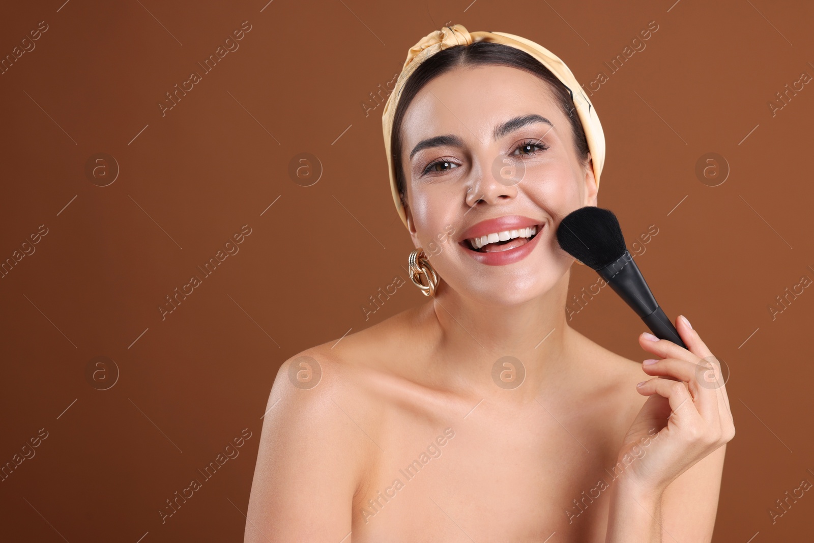 Photo of Beautiful woman applying makeup with brush on brown background, space for text