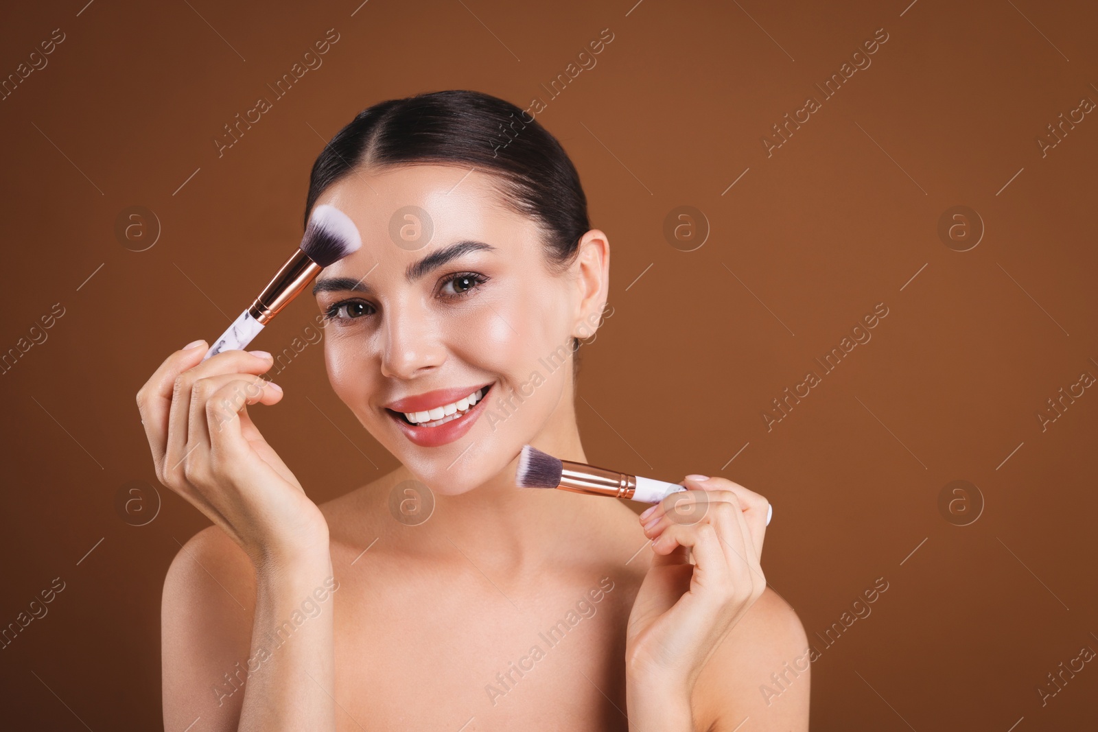 Photo of Beautiful woman with makeup brushes on brown background, space for text
