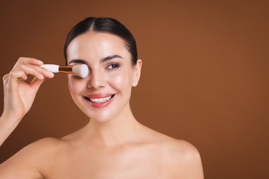 Photo of Beautiful woman with makeup brush on brown background, space for text