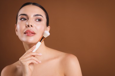 Photo of Beautiful woman with makeup brush on brown background, space for text
