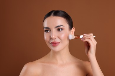 Photo of Beautiful woman applying makeup with brush on brown background