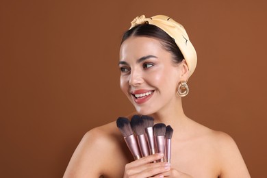 Photo of Beautiful woman with makeup brushes on brown background