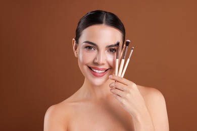 Photo of Beautiful woman with makeup brushes on brown background