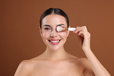 Photo of Beautiful woman with makeup brush on brown background