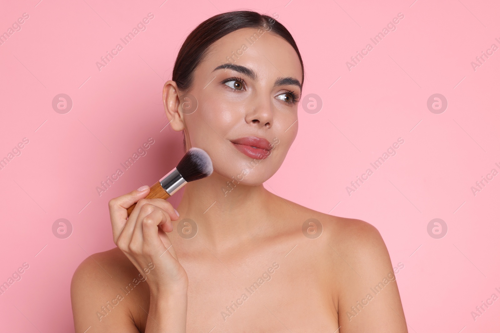 Beautiful woman applying makeup with brush on pink background Photo of Beautiful woman applying makeup with brush on pink background