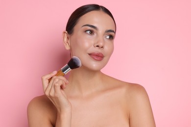Photo of Beautiful woman applying makeup with brush on pink background