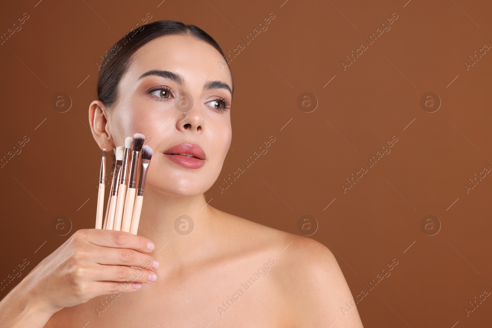 Photo of Beautiful woman with makeup brushes on brown background, space for text