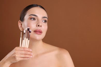 Photo of Beautiful woman with makeup brushes on brown background, space for text