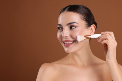 Photo of Beautiful woman applying makeup with brush on brown background, space for text