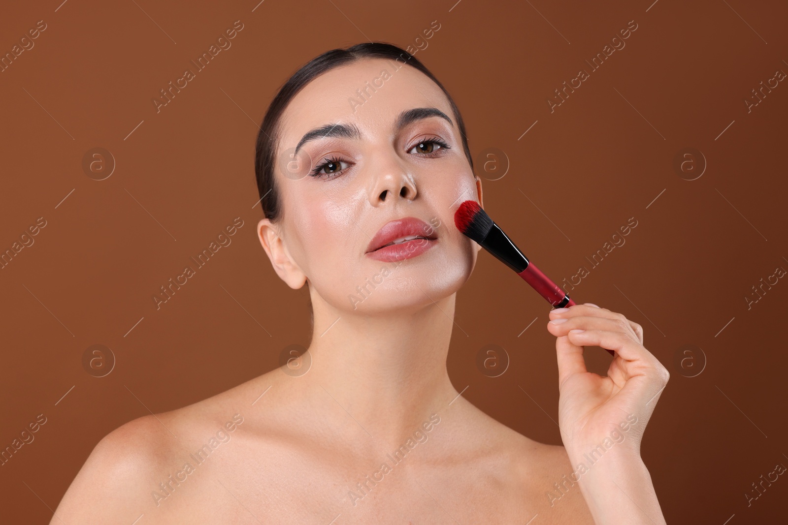 Photo of Beautiful woman applying makeup with brush on brown background