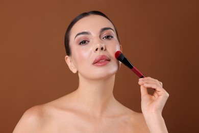 Photo of Beautiful woman applying makeup with brush on brown background