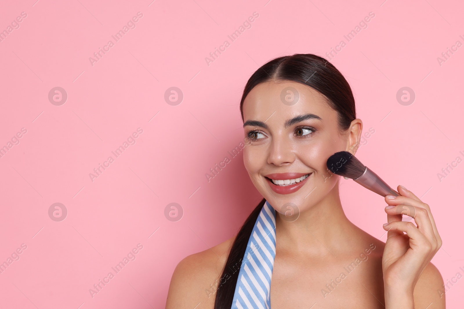 Photo of Beautiful woman applying makeup with brush on pink background, space for text