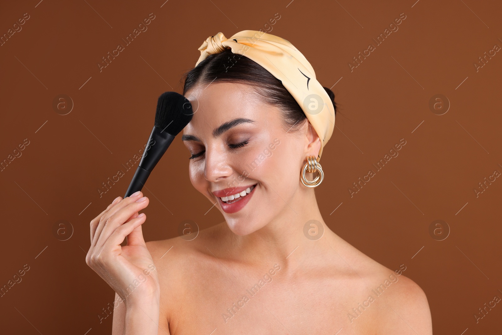 Beautiful woman applying makeup with brush on brown background Photo of Beautiful woman applying makeup with brush on brown background