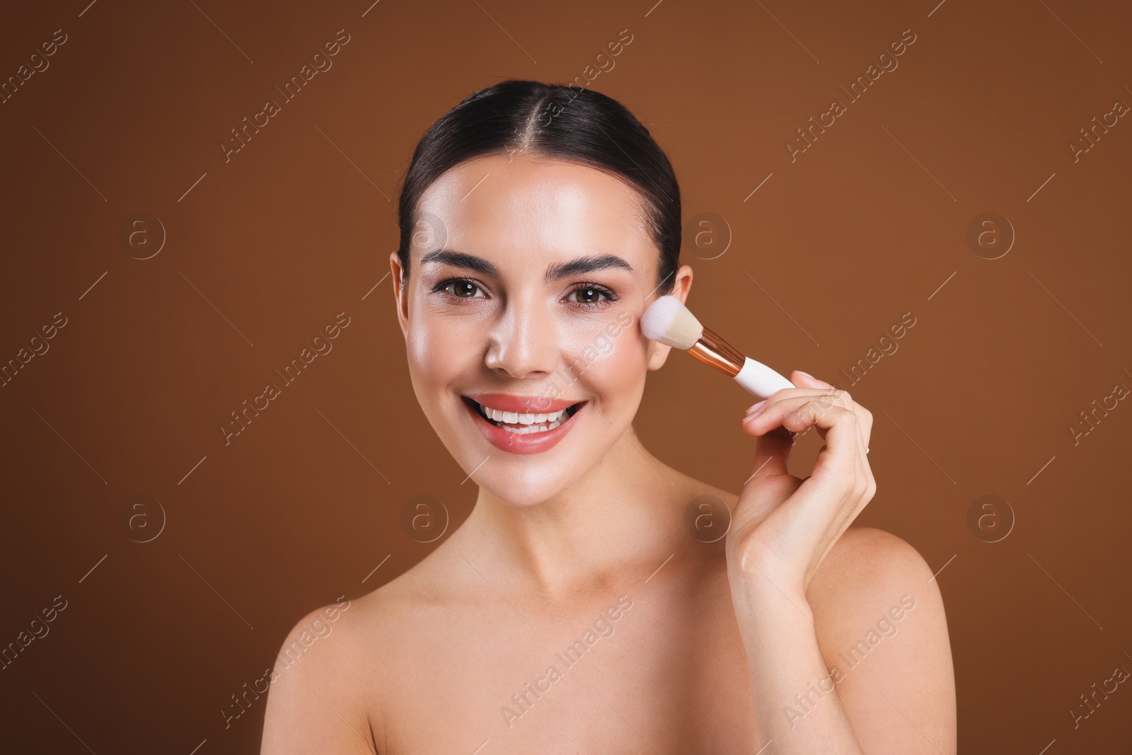 Photo of Beautiful woman applying makeup with brush on brown background