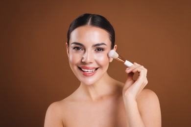 Photo of Beautiful woman applying makeup with brush on brown background