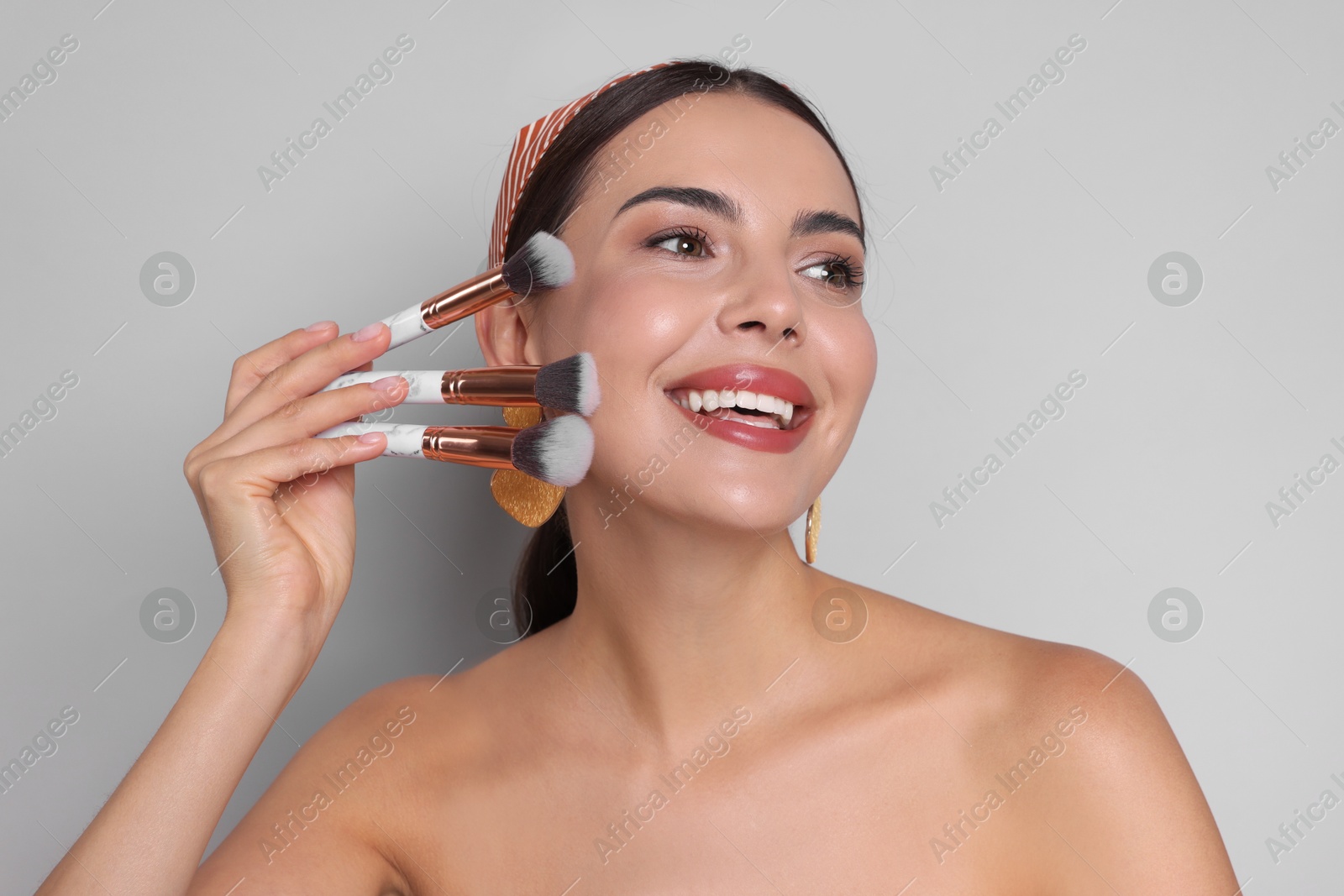 Photo of Beautiful woman with makeup brushes on light grey background