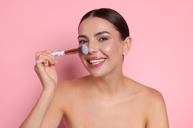 Photo of Beautiful woman applying makeup with brush on pink background