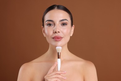 Photo of Beautiful woman with makeup brush on brown background