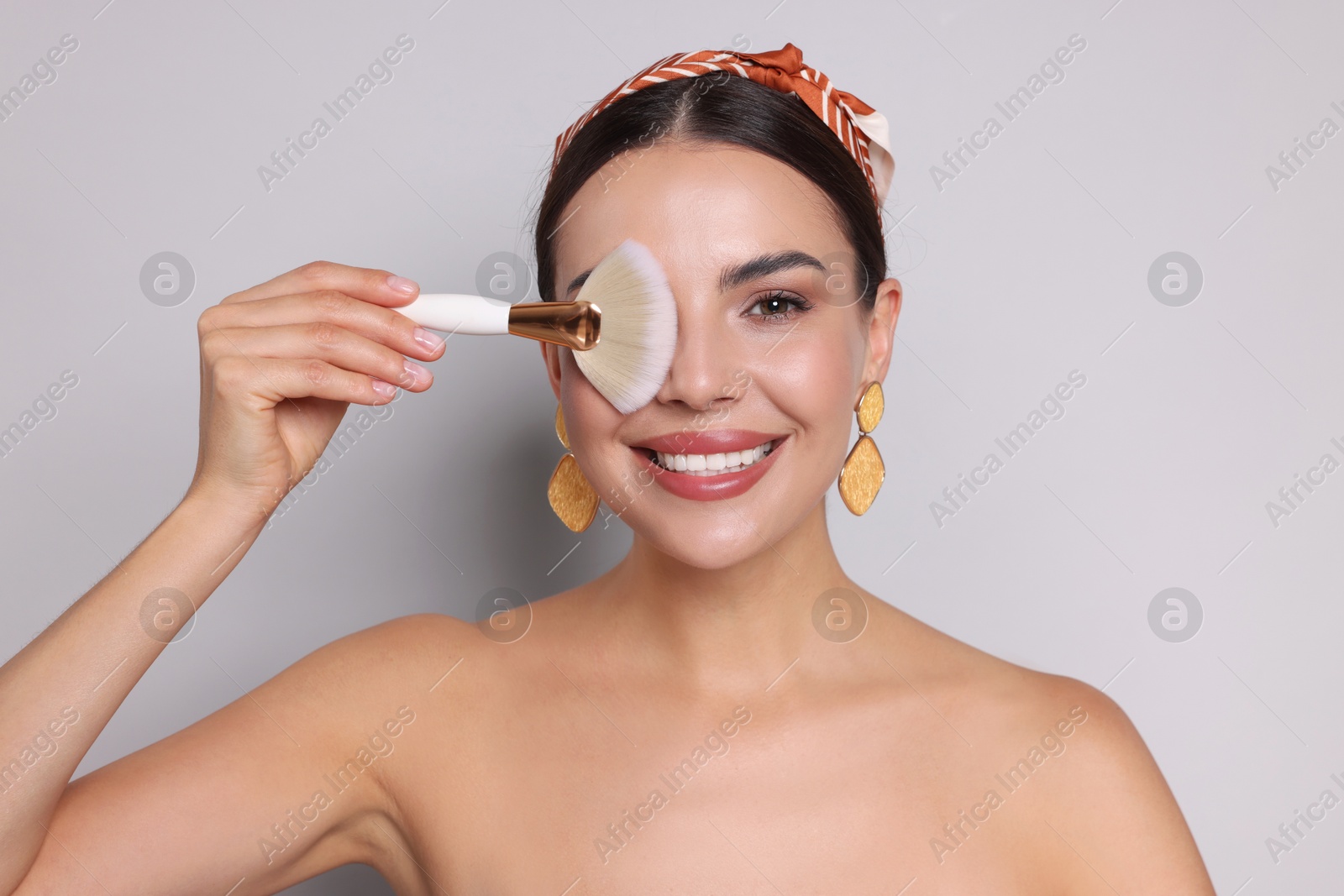 Beautiful woman with makeup brush on light grey background Photo of Beautiful woman with makeup brush on light grey background