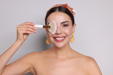 Photo of Beautiful woman with makeup brush on light grey background