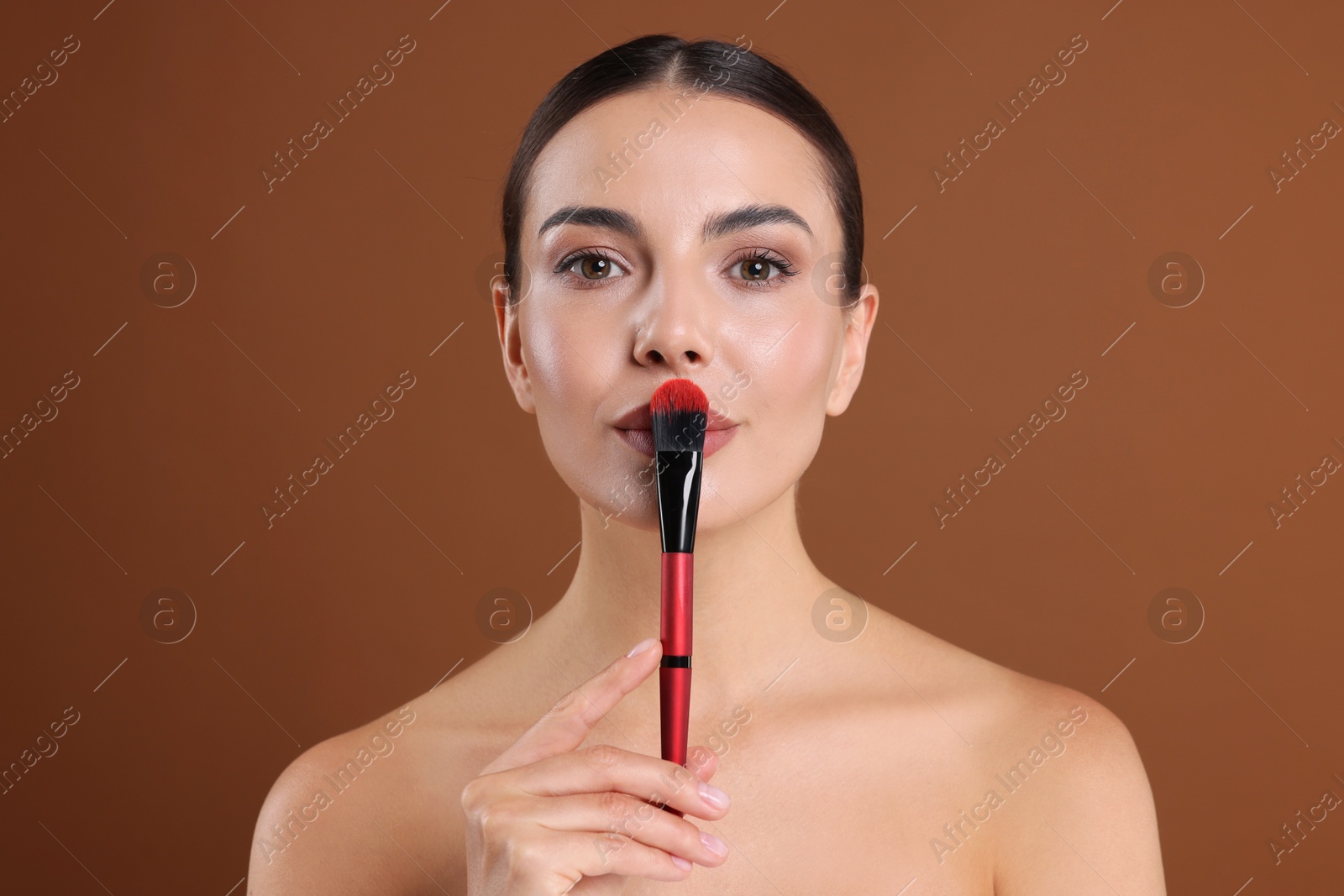 Beautiful woman with makeup brush on brown background Photo of Beautiful woman with makeup brush on brown background