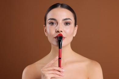 Photo of Beautiful woman with makeup brush on brown background