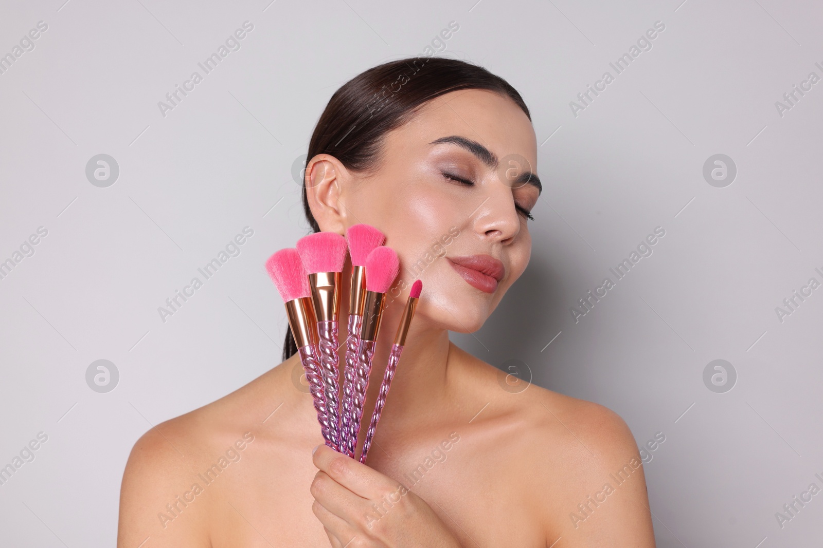 Photo of Beautiful woman with makeup brushes on light grey background