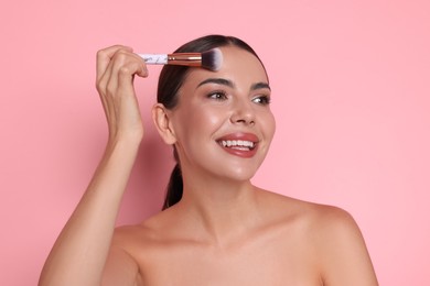Photo of Beautiful woman applying makeup with brush on pink background