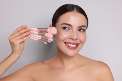 Photo of Beautiful woman with makeup brushes on light grey background