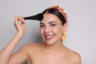 Photo of Beautiful woman applying makeup with brush on light grey background