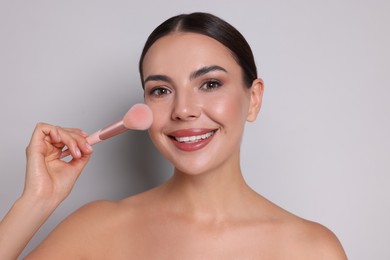 Photo of Beautiful woman applying makeup with brush on light grey background