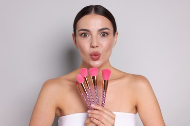 Photo of Beautiful woman with makeup brushes on light grey background
