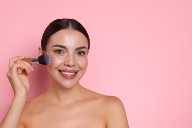 Photo of Beautiful woman applying makeup with brush on pink background, space for text
