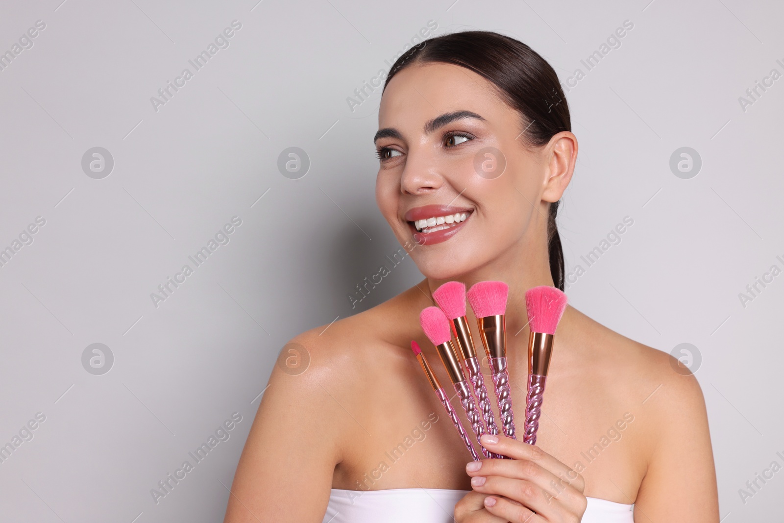 Beautiful woman with makeup brushes on light grey background, space for text Photo of Beautiful woman with makeup brushes on light grey background, space for text