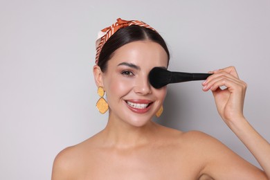 Photo of Beautiful woman with makeup brush on light grey background