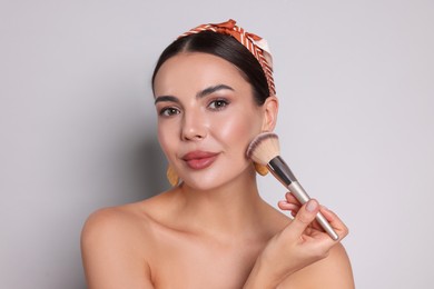 Photo of Beautiful woman applying makeup with brush on light grey background
